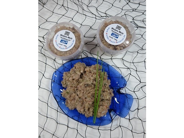 Matjes-Mett Knoblauch Matjes-Mett Knoblauch in Schale mit frischen Schnittlauchstängeln, darunter zwei Dosen Produkt.