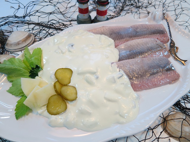 Matjesfilets in Sahnesauce auf weißem Teller, garniert mit Gurkenscheiben und Kräutern.