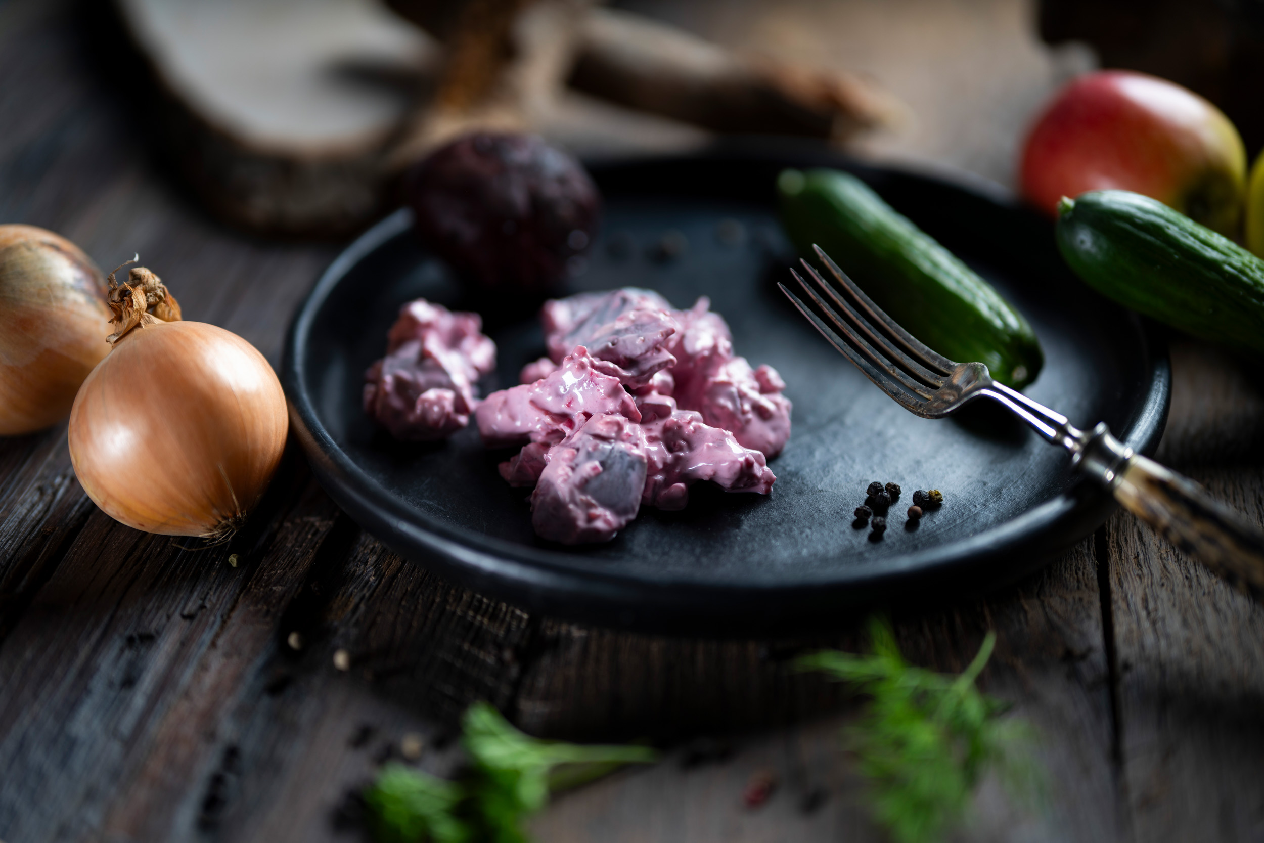 Roter Heringssalat  Roter Heringssalat in feiner Sahne-Sauce auf dunklem Teller mit roter Bete und Gurke dekoriert.