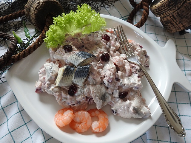 Usedomer Fischerschmaus Usedomer Fischsalat mit Matjes, Cranberries und Garnelen auf weißem Fisch-Teller, maritim serviert.