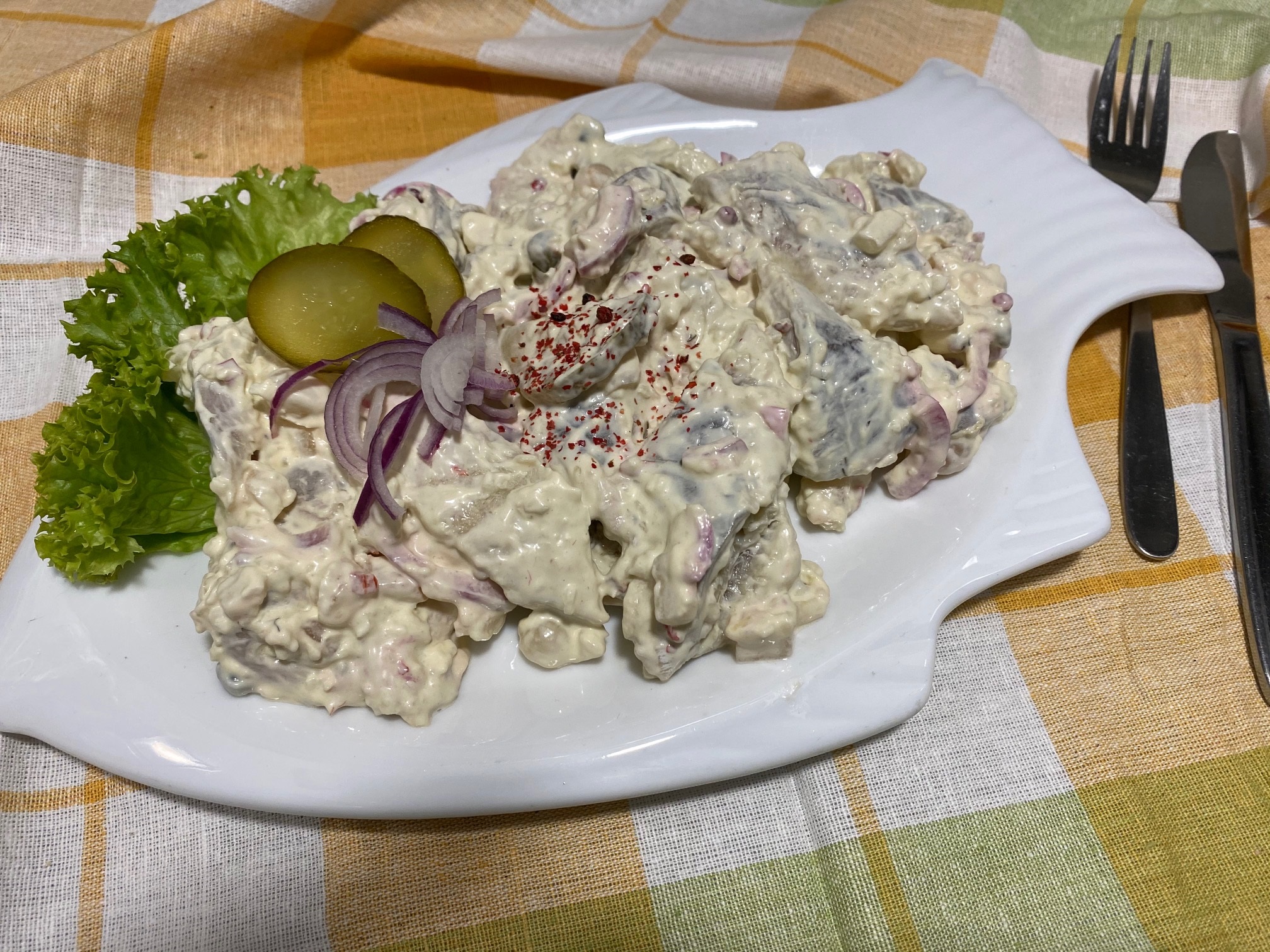 Greetsieler Heringstopf Cremiger Fischsalat mit Gurkenscheiben, roten Zwiebeln und Dill auf Tellerteller garniert.