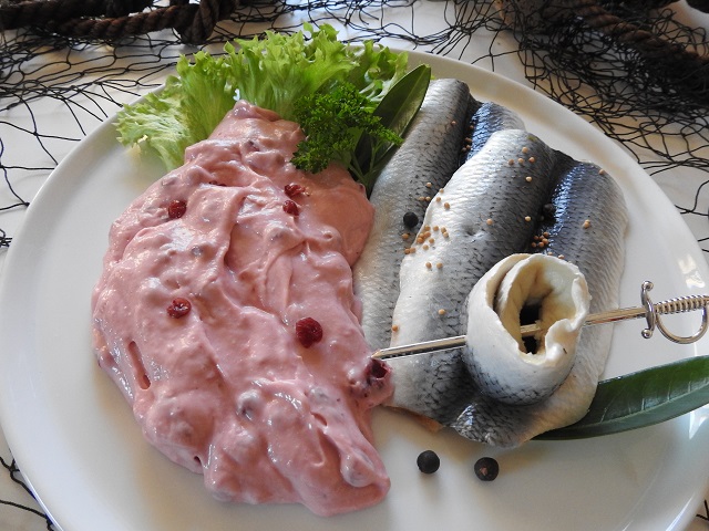Bismarckfilets mit rosa Preiselbeersahne auf Teller, garniert mit Salat, Lorbeerblatt & Kräutern.