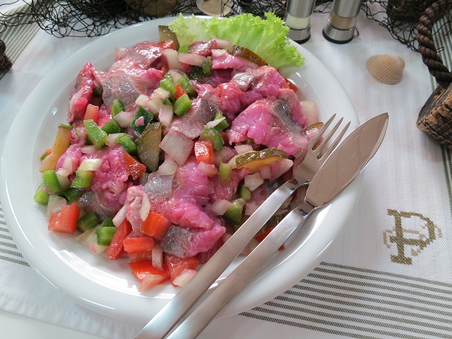 Kräutermatjes mit Paprika, Zwiebeln & Gurkenstücken auf weißem Teller, frisch angerichtet.