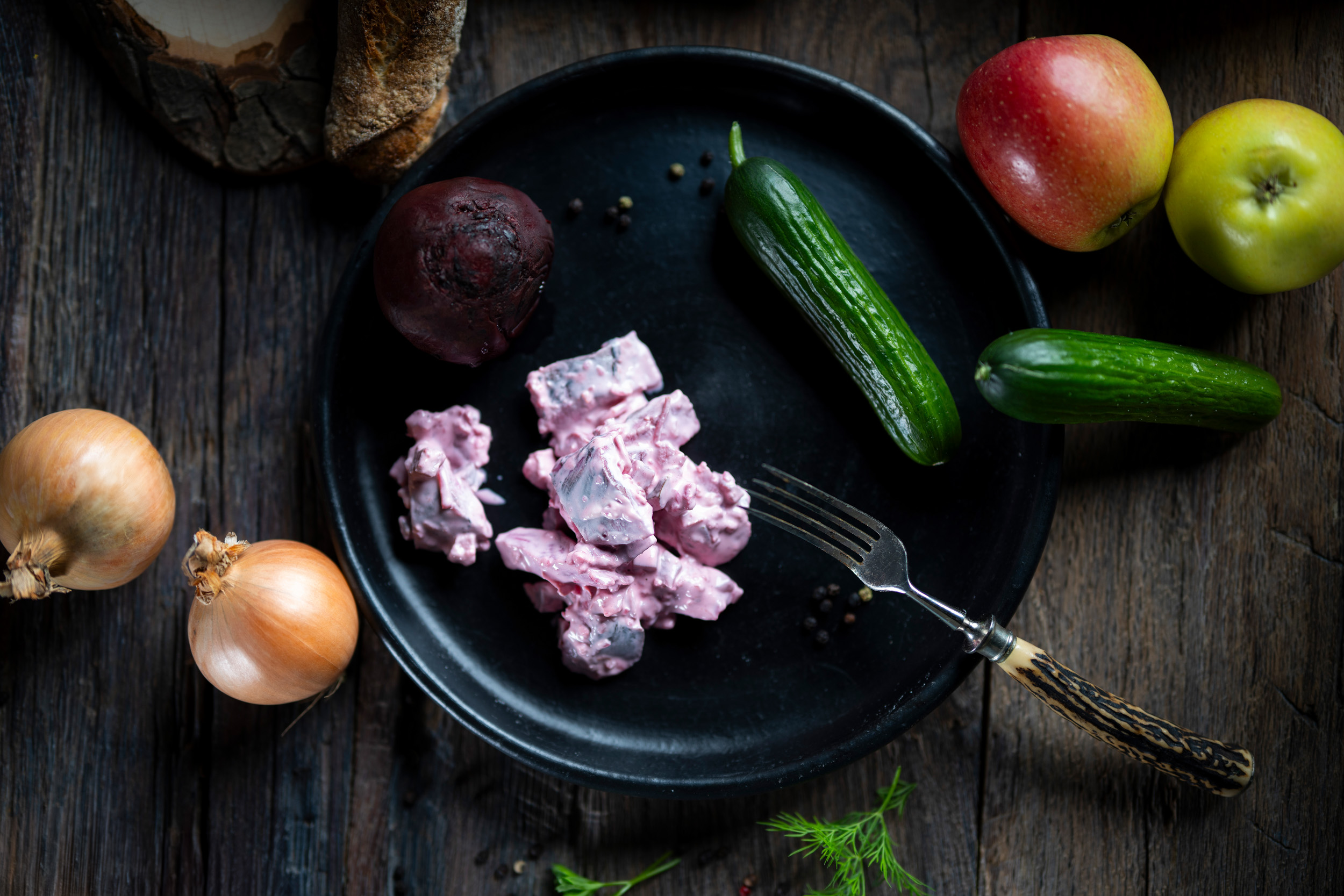 Roter Heringssalat  Roter Heringssalat in feiner Sahne-Sauce auf dunklem Teller mit roter Bete und Gurke dekoriert.