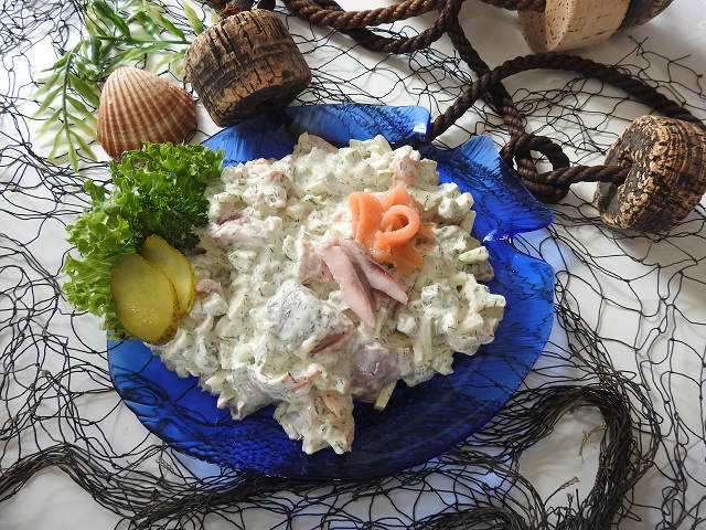 Nordlicht-Fischsalat mit Matjes und Gurke in cremiger Sauce, dekoriert auf blauem Teller — maritim.